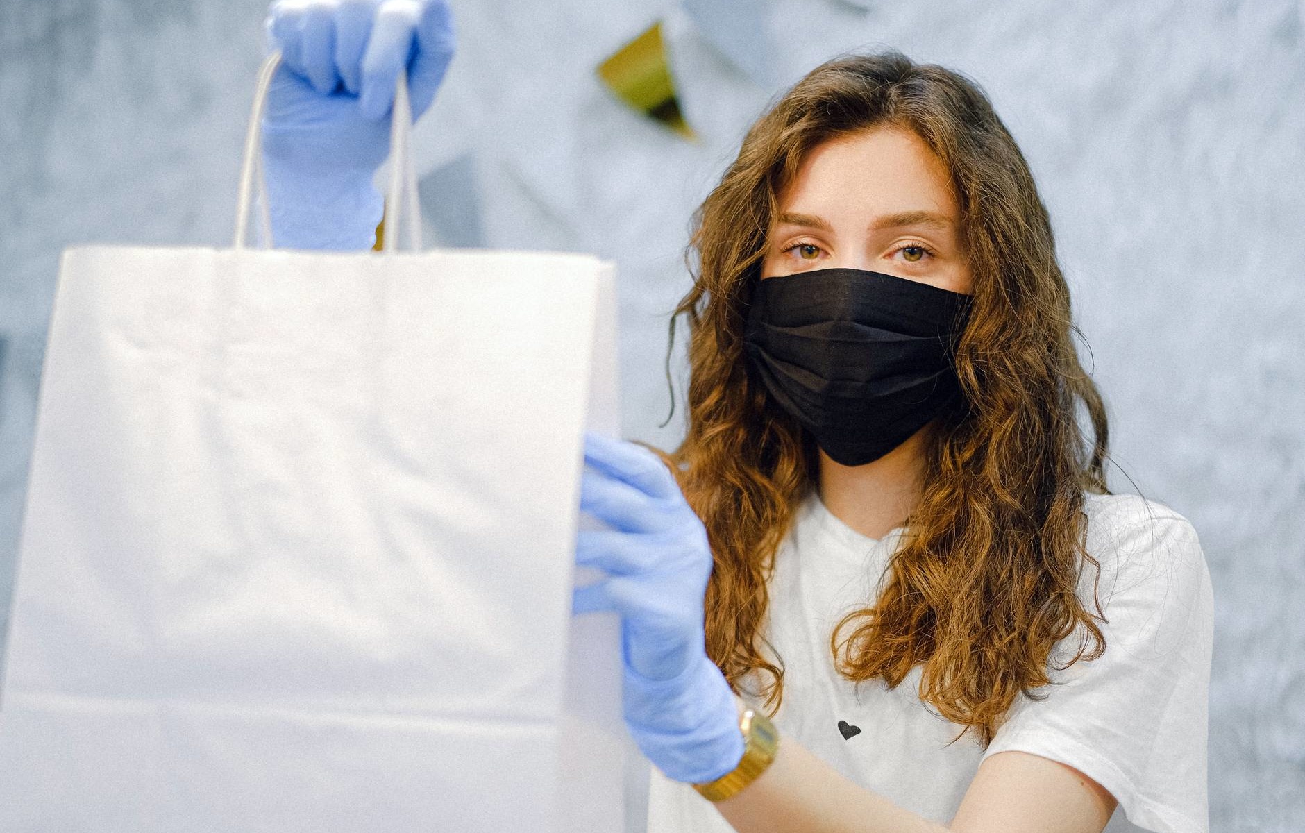 woman with face mask and latex gloves holding a shopping bag